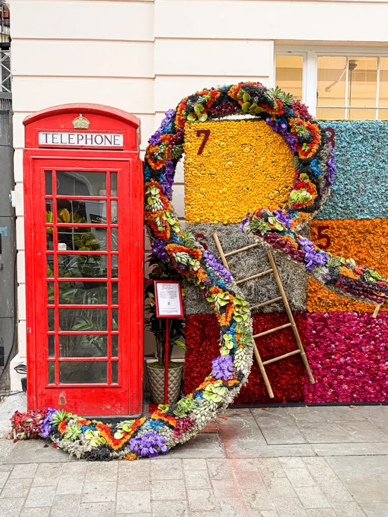 a red telephone box beside a large snake made of flowers against a floral playing board