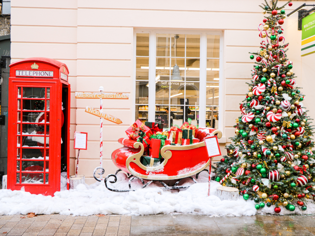 A red telephone box resting on fake snow, next to a red present filled sleigh, and big christmas tree in Belgravia