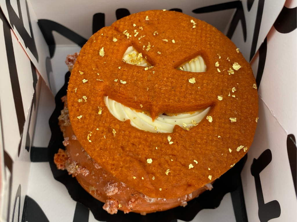 a pumpkin crumble doughnut with an orange sable in the shape of a carved pumpkin sat on top of cream