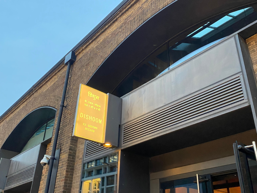 The outside of Dishoom in King's Cross - featuring a mustard yellow sign that say dishoom