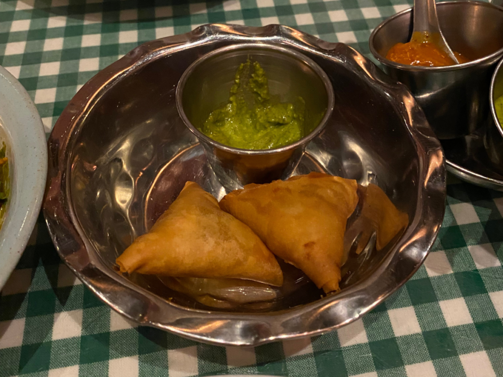 Vegetable samosas in a metal dish served with a green chutney