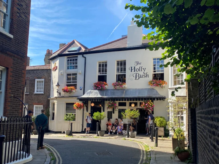 The London Eats List ultimate guide to Hampstead. Image shows a cute white pub down a pathway that says 'The Holly Bush'