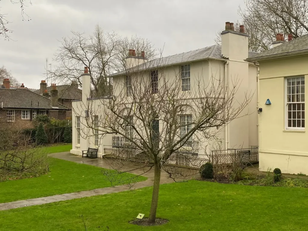 Keats House in Hampstead. An old cream building with two floors, a bare tree in front, with bright green grass