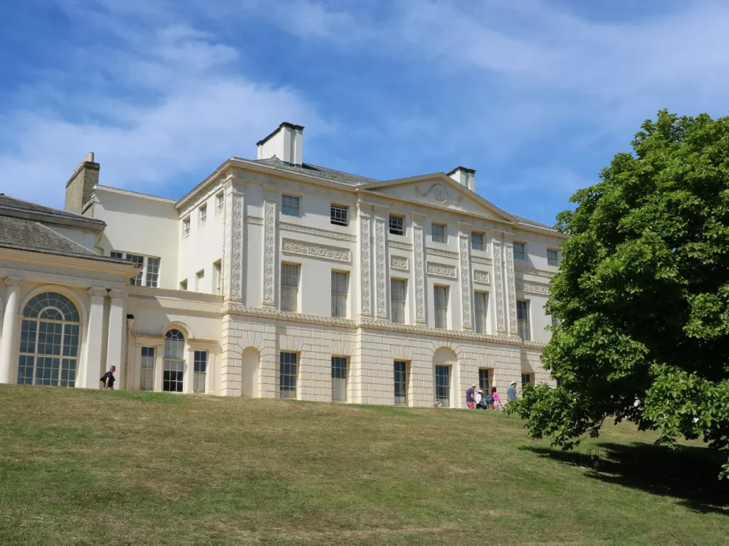 A large white mansion sat on top of a grassy hill against a blue sky background