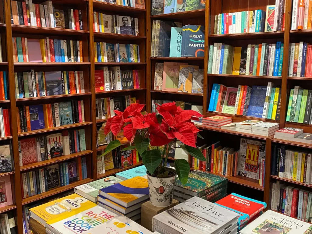 Inside Daunt Books in Hampstead - wooden bookshelves with a table in front holding a poinsettia 