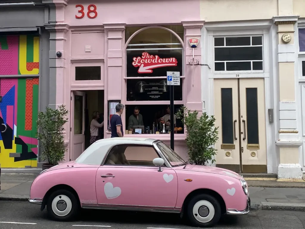 A small pink vintage car with a white roof and white hearts sits outside a pink cafe in Covent Garden