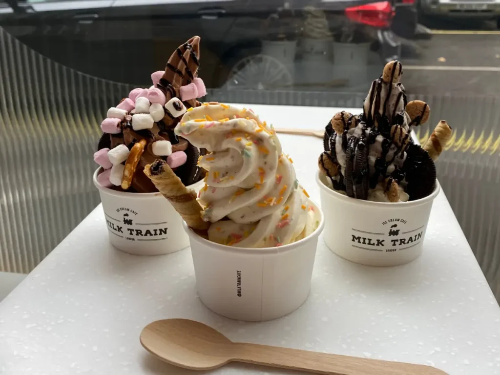 Three soft-serve ice creams with different toppings including pretzels. marshmallows and oreos